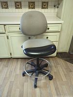 Full view of ErgoCentric drafting chair showing fabric backrest, padded seat, metal foot ring, caster base