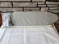 Full view of folded ironing board with gray cover and packaged holder