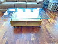 Full view of glass-top coffee table showing glass surface, wood base, casters