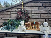Group shot showing nativity set, two angel figurines, wreath, garland and string lights on table