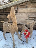 Front view of both woven reindeer standing on snow against stone wall