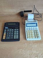 Both calculators side by side with adapter and paper roll visible