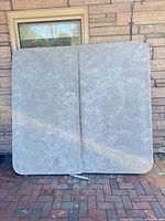 Front view of folded grey vinyl spa cover leaning against wall