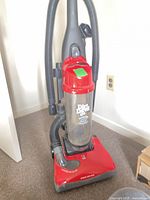 Front view of red Dirt Devil upright vacuum showing dust cup, hose and base