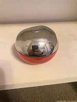 Chrome and red apple-shaped perfume bottle on white shelf