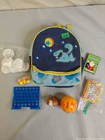Entire lot laid out: backpack, Connect 4 board, two card games, egg toy, orange ball