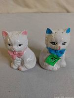 Front view of both porcelain cat shakers showing bows and vent holes