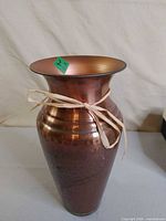 Full view of hammered copper vase with flared rim and raffia tie