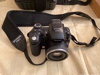Front view of Fujifilm FinePix S5000 camera with attached lens, strap and carry bag behind