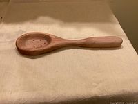 Top view of entire hand-carved wooden spoon showing bowl, drainage holes and handle