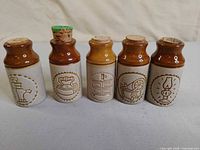 Front view of five miniature ceramic milk can bottles with different incised motifs and corks