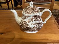 Side view of brown transferware Myott Coaching Days teapot with lid on wooden surface