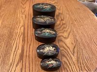Five lacquer boxes displayed in descending size order showing painted lids