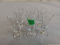 Six clear stemmed ouzo glasses arranged upright