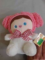 Front view of plush doll showing hair, bow, face and tag