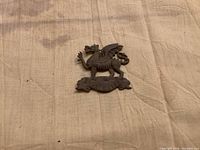 Front view of brass dragon cap badge with scroll "THE BUFFS"