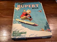 Front cover showing title 'The Rupert Book', illustration of Rupert on skis
