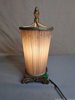 Full view of lit vintage table lamp showing metal base, pleated shade, prisms, finial, cord
