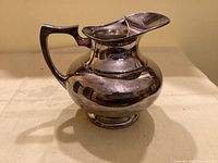 Full view of silver-plated pitcher showing shape, handle, spout and pedestal