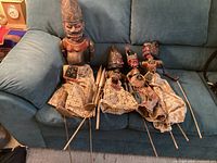Four Wayang Golek rod puppets laid on sofa showing size difference, carved heads, rods, costumes