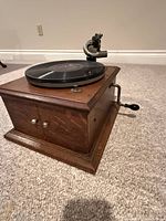 Wood cabinet gramophone with hand crank inserted, tonearm and platter visible