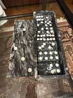 Black marble-effect domino tiles arranged in open rectangular tray with matching lid