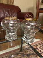 Two clear glass votive holders with gold rims on glass table