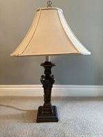 Full view of lamp showing bronze base, ornate carvings, beige bell shade, and finial