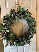 Front view of artificial evergreen wreath with pinecones, eucalyptus, and lights hung on door