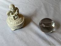 Porcelain cherub trinket box and clear crystal baseball paperweight side by side