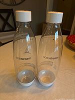 Two clear SodaStream 1L bottles with white caps and bases standing side by side on table