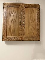 Front view of closed solid oak dartboard cabinet showing wood grain, brass pulls and hinges