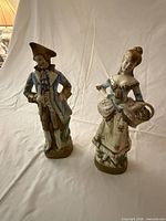 Full view of both porcelain figurines standing on cloth backdrop