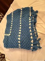 Folded blue crocheted throw with white tasselled stripes