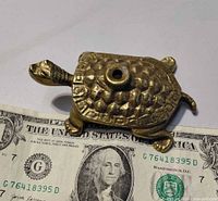 Top view of brass turtle paperweight beside US dollar bill for scale