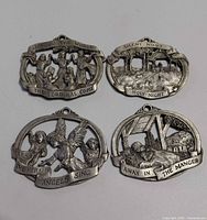 Front view of all four pewter ornaments displaying scenes and inscriptions