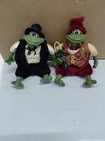 Front view of both Mr. Pondhopper frog figurines displaying outfits and accessories