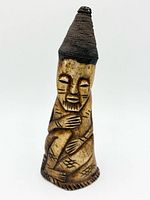 Front view of carved bone figure showing facial features, body posture and woven cap