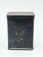 front view of black metal tin showing overall form and patina