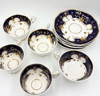 five teacups and stack of saucers showing interior cobalt and gilt pattern