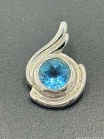 Front view of sterling silver pendant showing blue topaz and swirl design