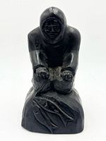 Front view of black cast resin Inuit hunter figurine kneeling over two fish