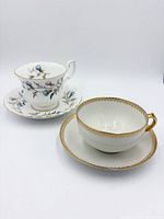 Gold lattice band teacup and saucer beside blue thistle floral teacup and saucer