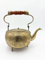 front view of etched copper teapot showing floral design, spout, feet, and wood-grip handle