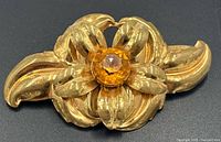 Front view of gold-tone flower brooch highlighting citrine glass center and layered petals