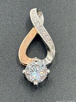 Front view of pendant showing two-tone swirl, pavé accents, solitaire stone