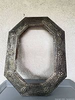 Front view of octagonal metal frame showing embossed floral pattern and silver-tone finish