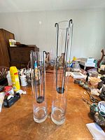 Full view of both tall glass cylinder vases with black metal hanger inserts standing on table