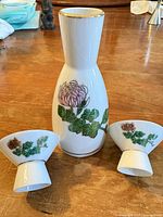 Front view of bottle and two cups showing floral design and gold rims