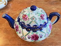 overall view showing floral decoration, cobalt blue trim and chip on spout